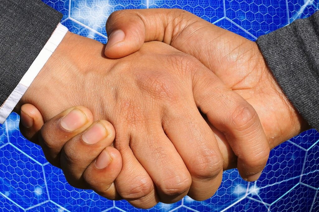 Two business owners shaking hands across a conference table after agreeing the terms of a contingent earn-out payment.